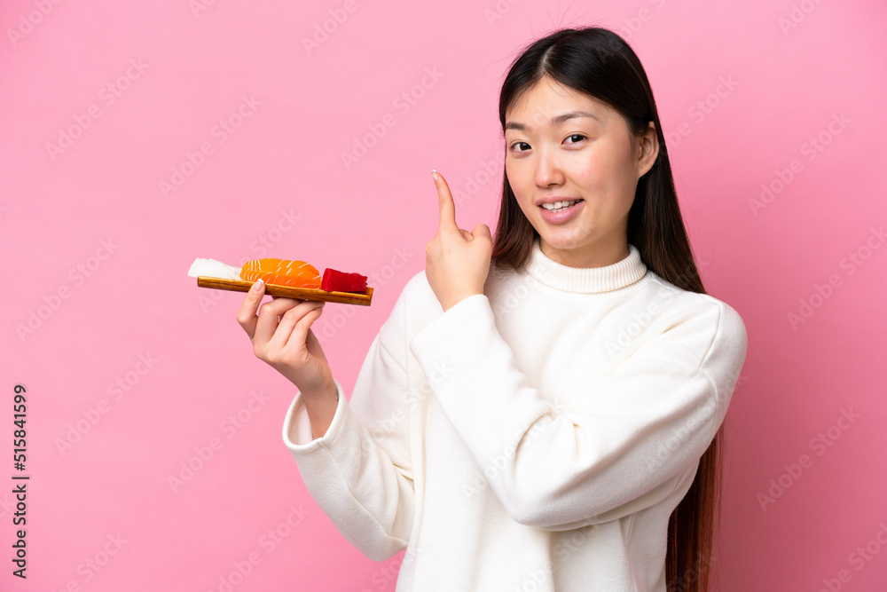 Young Chinese woman holding sashimi isolated on pink background pointing back Young Chinese woman holding sashimi isolated on pink background pointing back