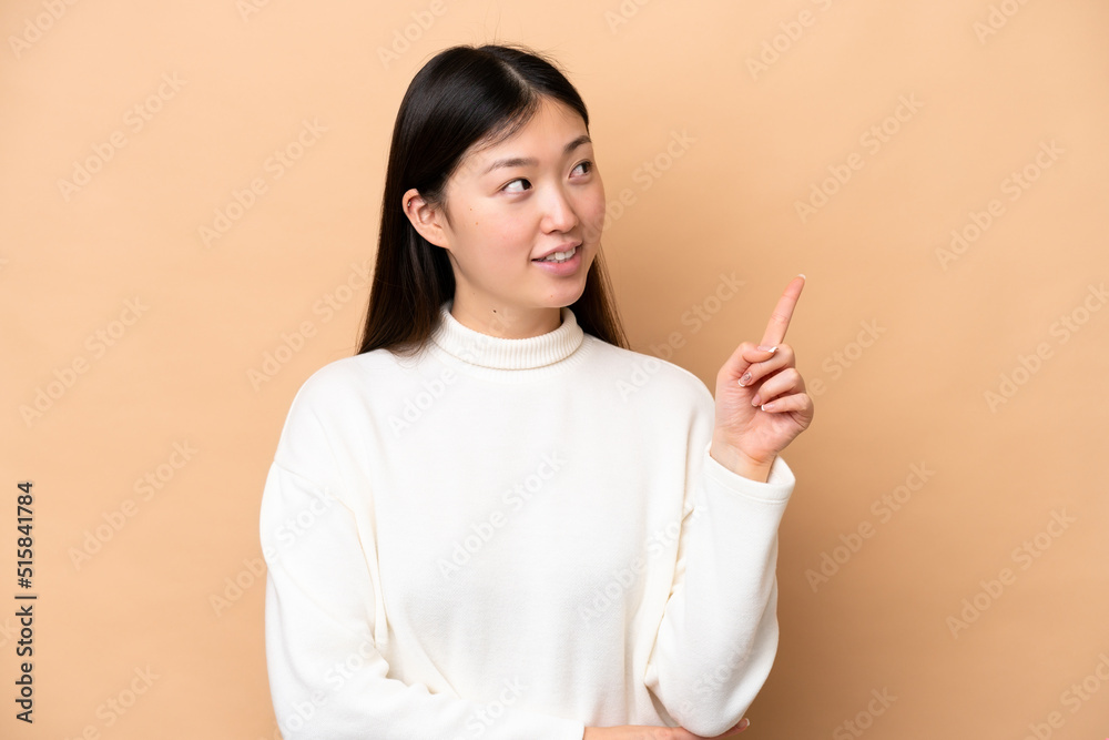 Young Chinese woman isolated on beige background pointing up a great idea Young Chinese woman isolated on beige background pointing up a great idea