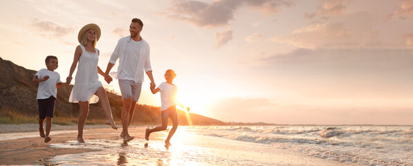 Happy family running on sandy beach near sea at sunset, space for text. Banner design