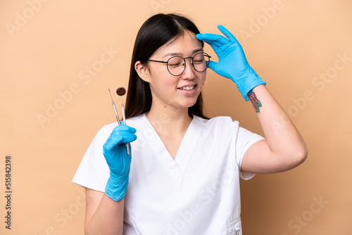 Dentist Chinese woman holding tools isolated on beige background smiling a lot