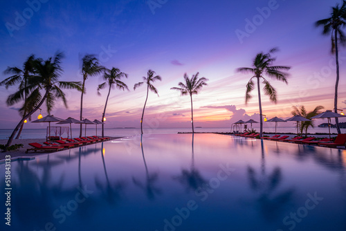 Outdoor luxury sunset over infinity pool swimming summer beachfront hotel resort, tropical landscape. Beautiful tranquil beach holiday vacation background. Amazing island sunset beach view, palm trees © icemanphotos