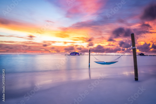 Fototapeta Naklejka Na Ścianę i Meble -  Tropical beach sunset as summer landscape with luxury resort beach swing or hammock and water villas and calm sea sky for sunset beach landscape. Tranquil beach scenery vacation and summer holiday