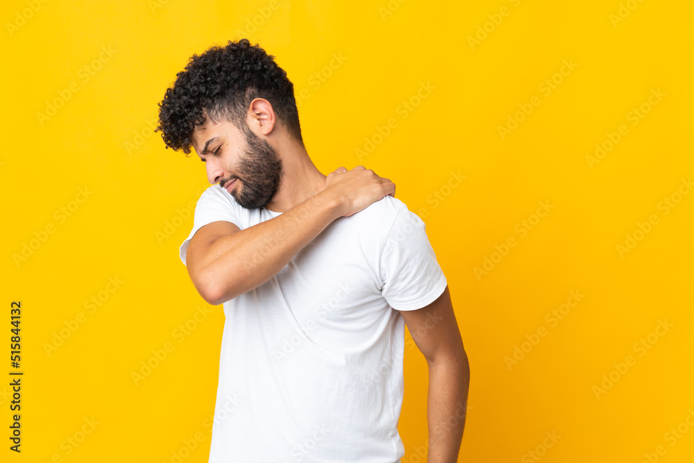 Young Moroccan man isolated on yellow background suffering from pain in shoulder for having made an effort Young Moroccan man isolated on yellow background suffering from pain in shoulder for having made an effort