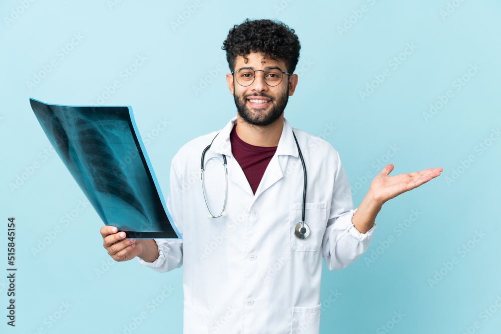 Young Moroccan traumatologist in workplace isolated on blue background with shocked facial expression Young Moroccan traumatologist in workplace isolated on blue background with shocked facial expression