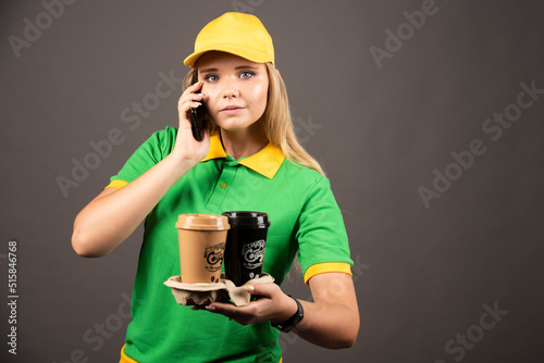 Deliverywoman with cups of coffee speaking on smartphone