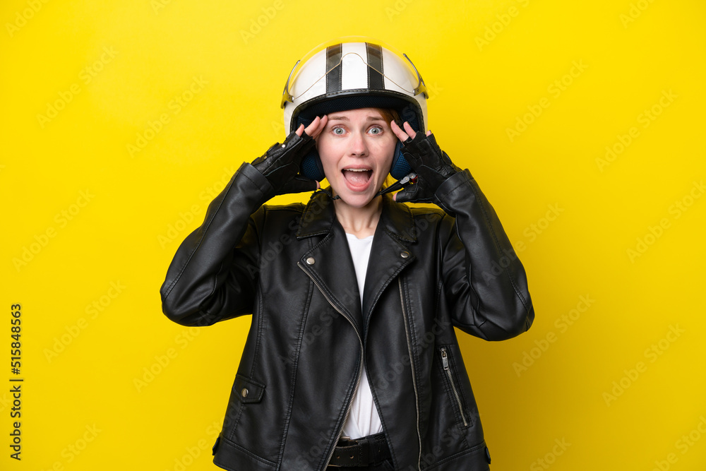 Young English woman with a motorcycle helmet isolated on yellow background with surprise expression Young English woman with a motorcycle helmet isolated on yellow background with surprise expression
