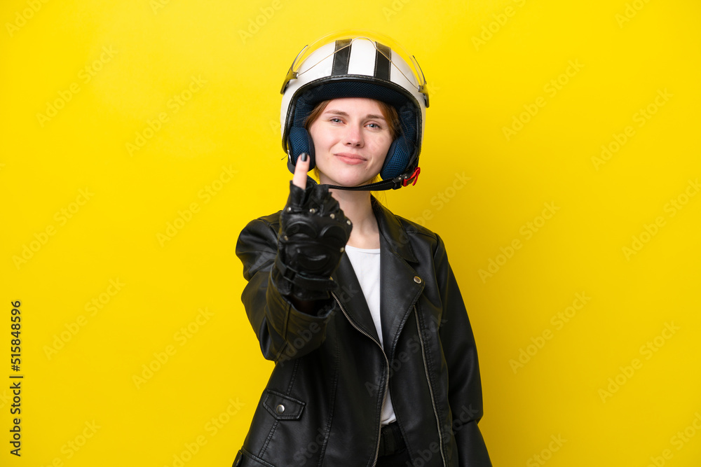 Young English woman with a motorcycle helmet isolated on yellow background doing coming gesture Young English woman with a motorcycle helmet isolated on yellow background doing coming gesture