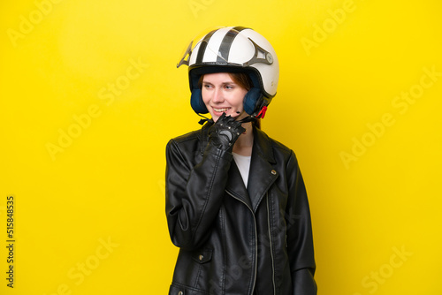 Young English woman with a motorcycle helmet isolated on yellow background looking to the side and smiling