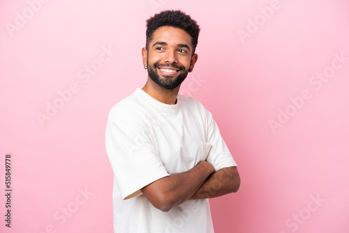 Young Brazilian man isolated on pink background with arms crossed and happy
