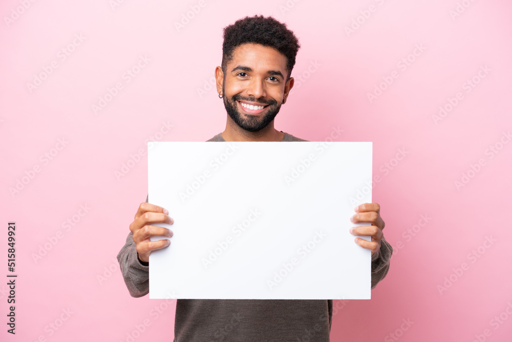 Young Brazilian man isolated on pink background holding an empty placard with happy expression Young Brazilian man isolated on pink background holding an empty placard with happy expression