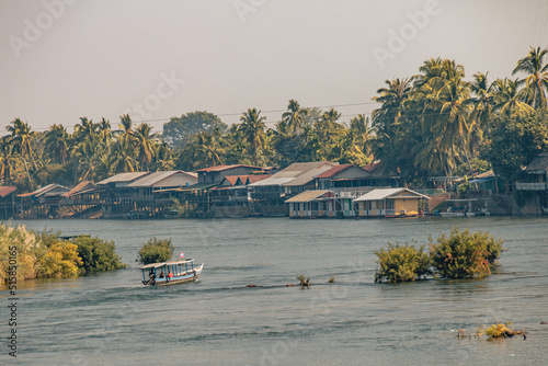 Don Det, Laos - January 18th, 2021 : View on the Mekong in the 4000 islands in the south of Laos with a tourist boat on the water and houses on the banks of the river.