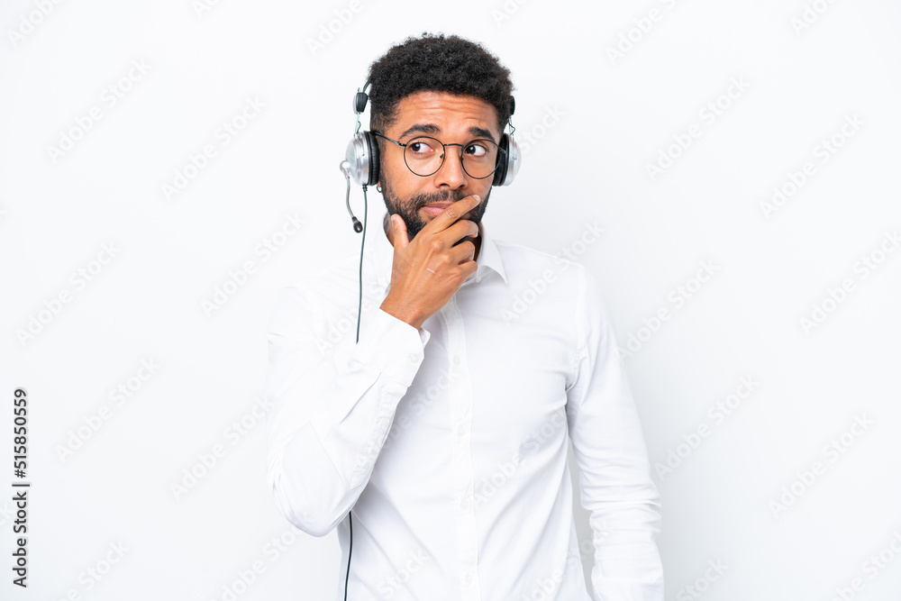 Telemarketer Brazilian man working with a headset isolated on white background having doubts and with confuse face expression Telemarketer Brazilian man working with a headset isolated on white background having doubts and with confuse face expression
