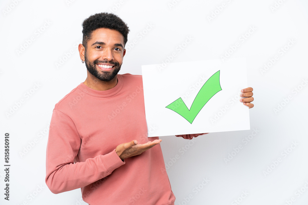 Young Brazilian man isolated on white background holding a placard with text Green check mark icon and pointing it Young Brazilian man isolated on white background holding a placard with text Green check mark icon and pointing it