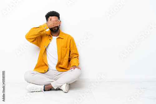 Young Brazilian man sitting on the floor isolated on white background covering eyes by hands. Do not want to see something
