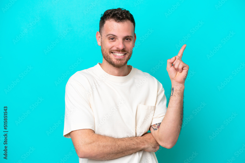 Young Brazilian man isolated on blue background happy and pointing up