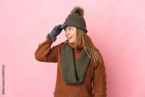 Middle age woman with winter hat isolated on pink background doing surprise gesture while looking to the side