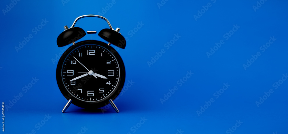 Black alarm clock on blue background, importance of time concept and time work.