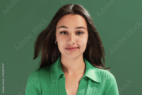 Portrait of beautiful young girl attentively looking at camera, posing isolated over green studio background