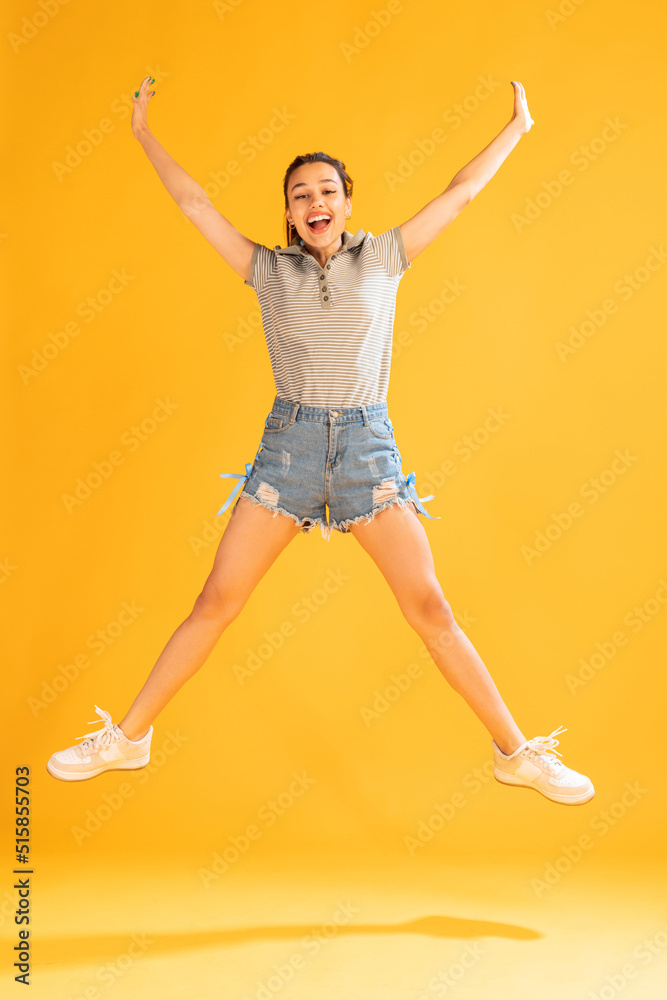 Portrait of beautiful young girl in casual outfit jumping, posing isolated over yellow studio background. Happiness