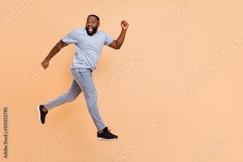 Full length body size view of attractive cheerful sportive guy jumping having fun running isolated over beige pastel color background