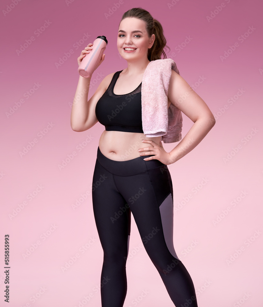 Sporty girl with towel after training. Photo of pretty model with curvy figure in black sportswear on pink background. Sports motivation and healthy lifestyle Sporty girl with towel after training. Photo of pretty model with curvy figure in black sportswear on pink background. Sports motivation and healthy lifestyle