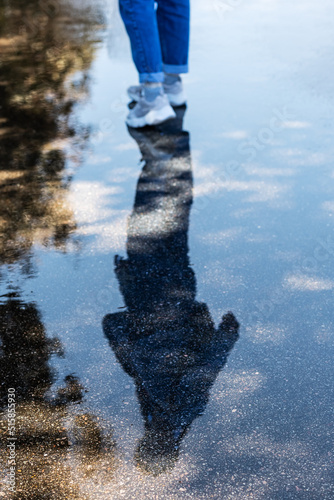 The silhouette of a walking woman is reflected in a puddle on wet pavement. Walk after the rain. Selective focus.