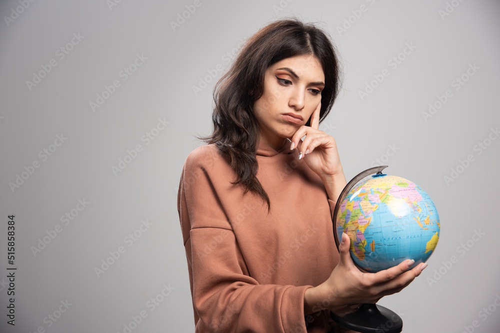 Serious looking woman looking at globe on gray background Serious looking woman looking at globe on gray background