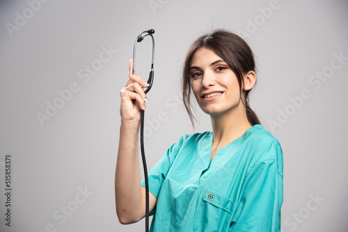 Happy doctor showing stethoscope on gray background