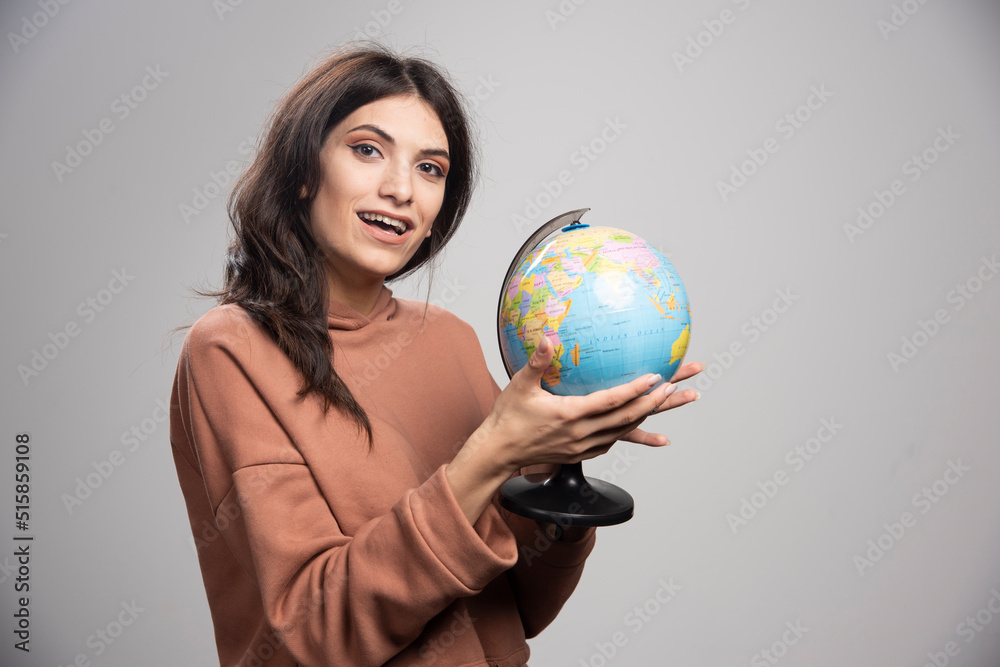 Brunette woman holding globe on gray background Brunette woman holding globe on gray background