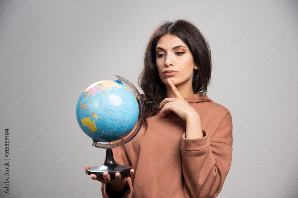 Brunette woman looking at globe on gray background Brunette woman looking at globe on gray background