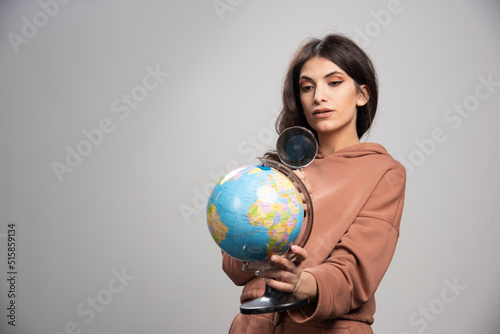 Brunette woman looking at globe with magnifying glass