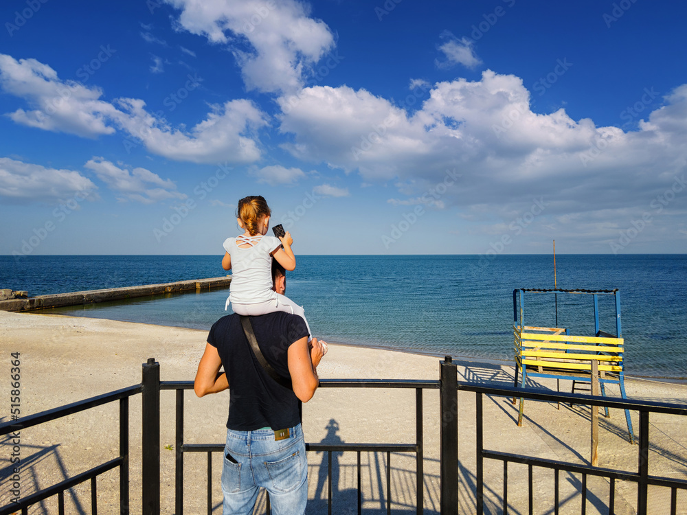 Dad with a daughter on his shoulders, against the backdrop of the sea