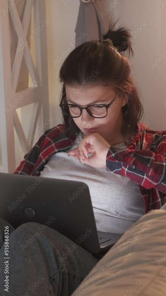 Vertical video. Remote job. Freelancer lifestyle. Digital business. Serious smart woman working from home online using laptop on couch.
