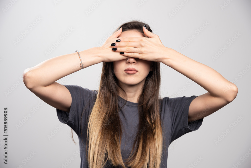 Young woman covering her eyes with hands over a gray background Young woman covering her eyes with hands over a gray background