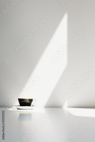 A black porcelain coffe cup on a white table with strong sunlight hitting the wall behind it. Nr.4 photo