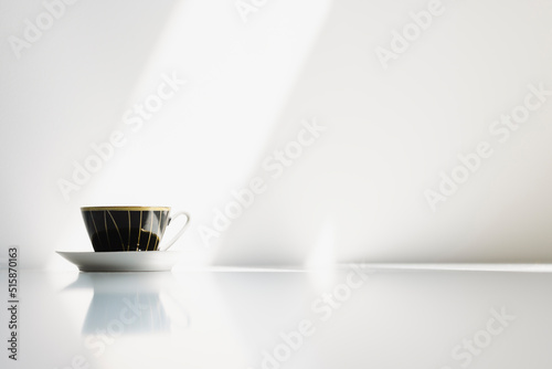 A black porcelain coffe cup on a white table with strong sunlight hitting the wall behind it. Nr.10 photo