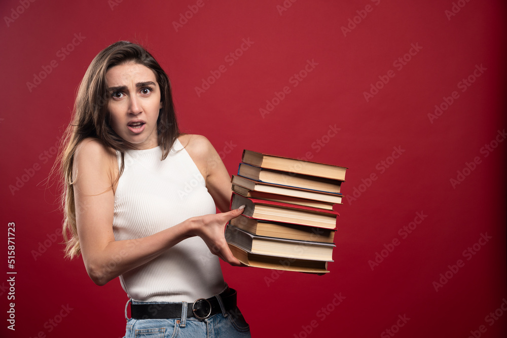 Portrait of a young student woman carrying lots of books on a red background Portrait of a young student woman carrying lots of books on a red background
