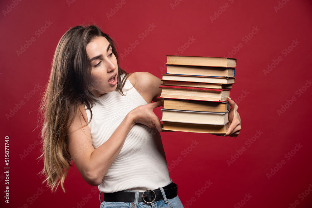 Young girl student holds a stack of books on a red background Young girl student holds a stack of books on a red background