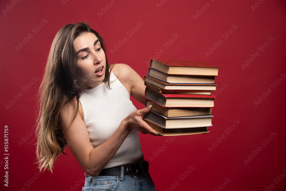 Young pretty woman model carrying a lot of books on a red background Young pretty woman model carrying a lot of books on a red background