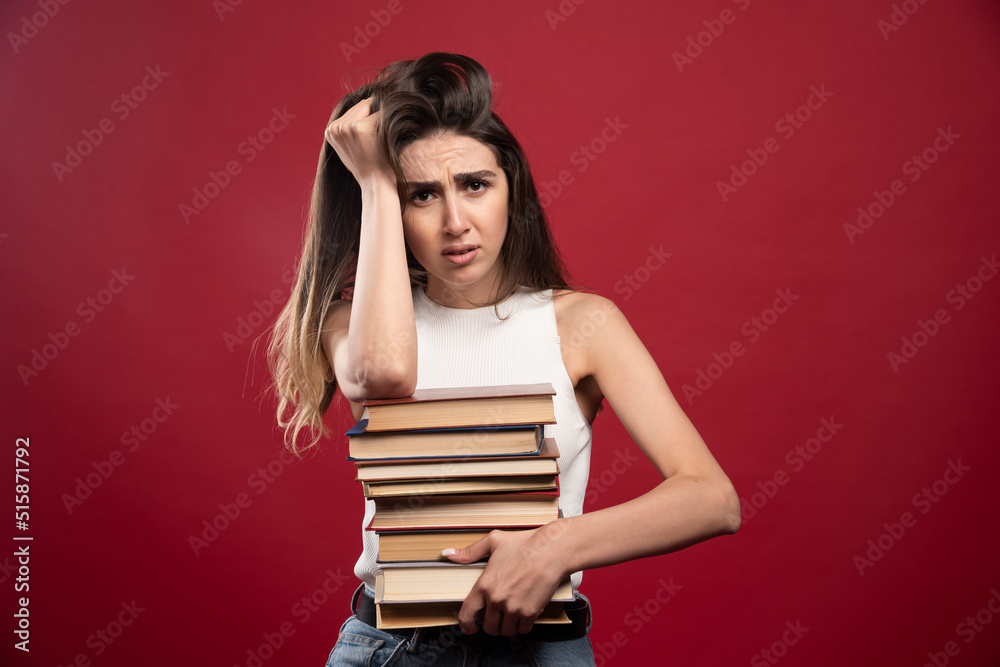 Portrait of a young brunette woman holding lots of books on a red background Portrait of a young brunette woman holding lots of books on a red background