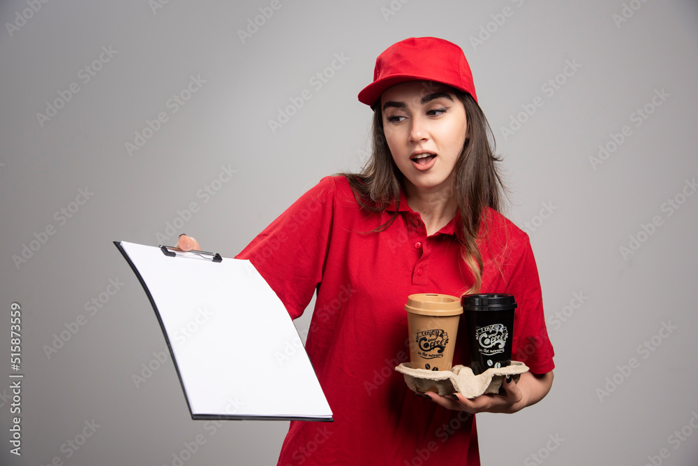 Delivery woman holding coffee cups and looking at clipboard Delivery woman holding coffee cups and looking at clipboard