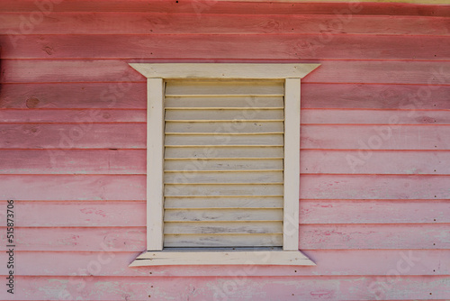 Rustic yellow and pink wooden house with wooden shutters. Dominican Republic.
