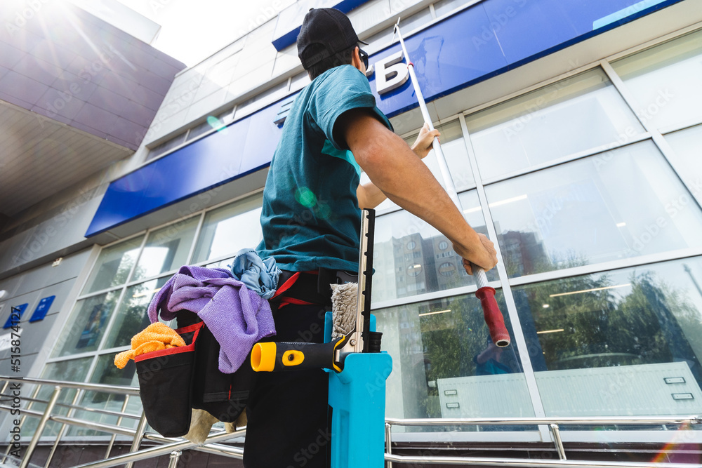 Male professional cleaning service worker in overalls cleans the windows and shop windows of a store with special equipment