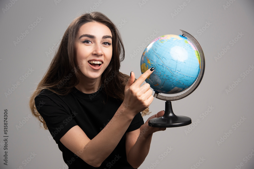 Happy woman pointing at globe on gray background Happy woman pointing at globe on gray background