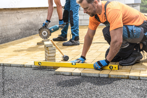 The worker's hand holds a spirit level while measuring the flatness of the interlocking pavement.