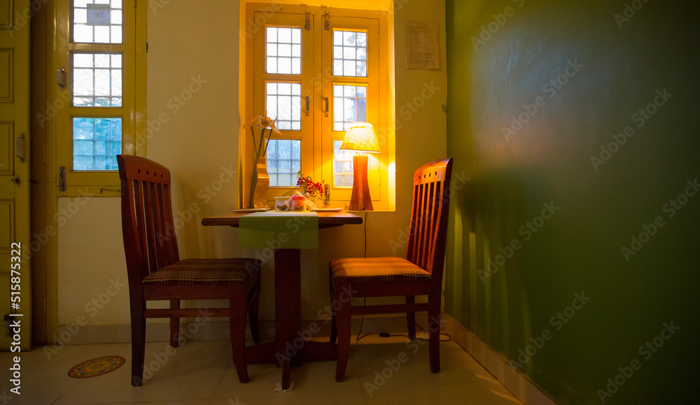 Beautiful cozy European interior in an Indian restaurant. A small table and two chairs near the window inside the cafe. Interior with warm light of table lamp. Home cooking