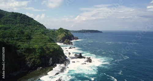 Slow forward flight along coastline of Siung Beach and agricultural plantation growing on hill photo