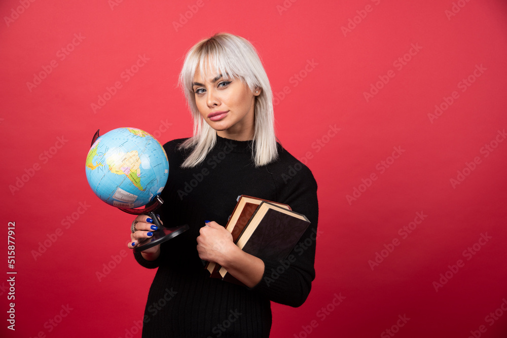 Young woman model posing with a books and a Earth globe on a red background Young woman model posing with a books and a Earth globe on a red background