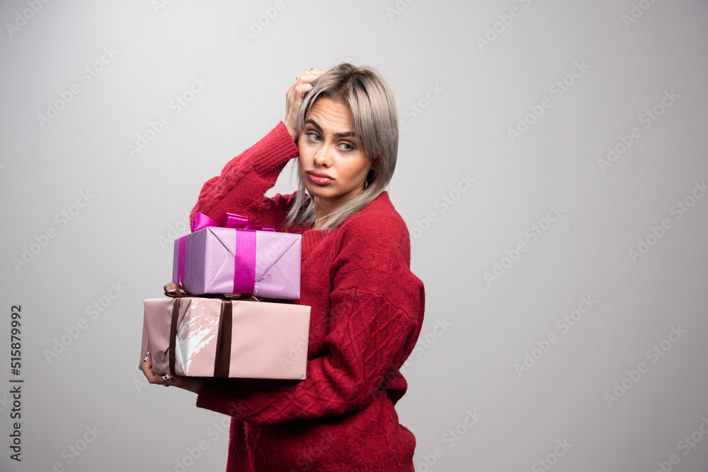 Portrait of sad woman holding gift boxes on gray background Portrait of sad woman holding gift boxes on gray background