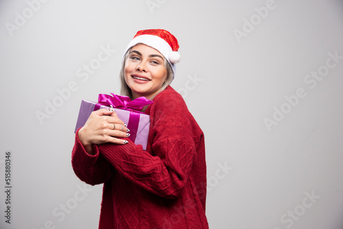 Happy woman in Santa hat hugs Christmas gift